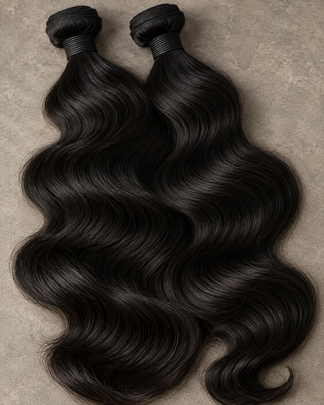 Illustrative black wavy hair bundles laid on warm grey stone